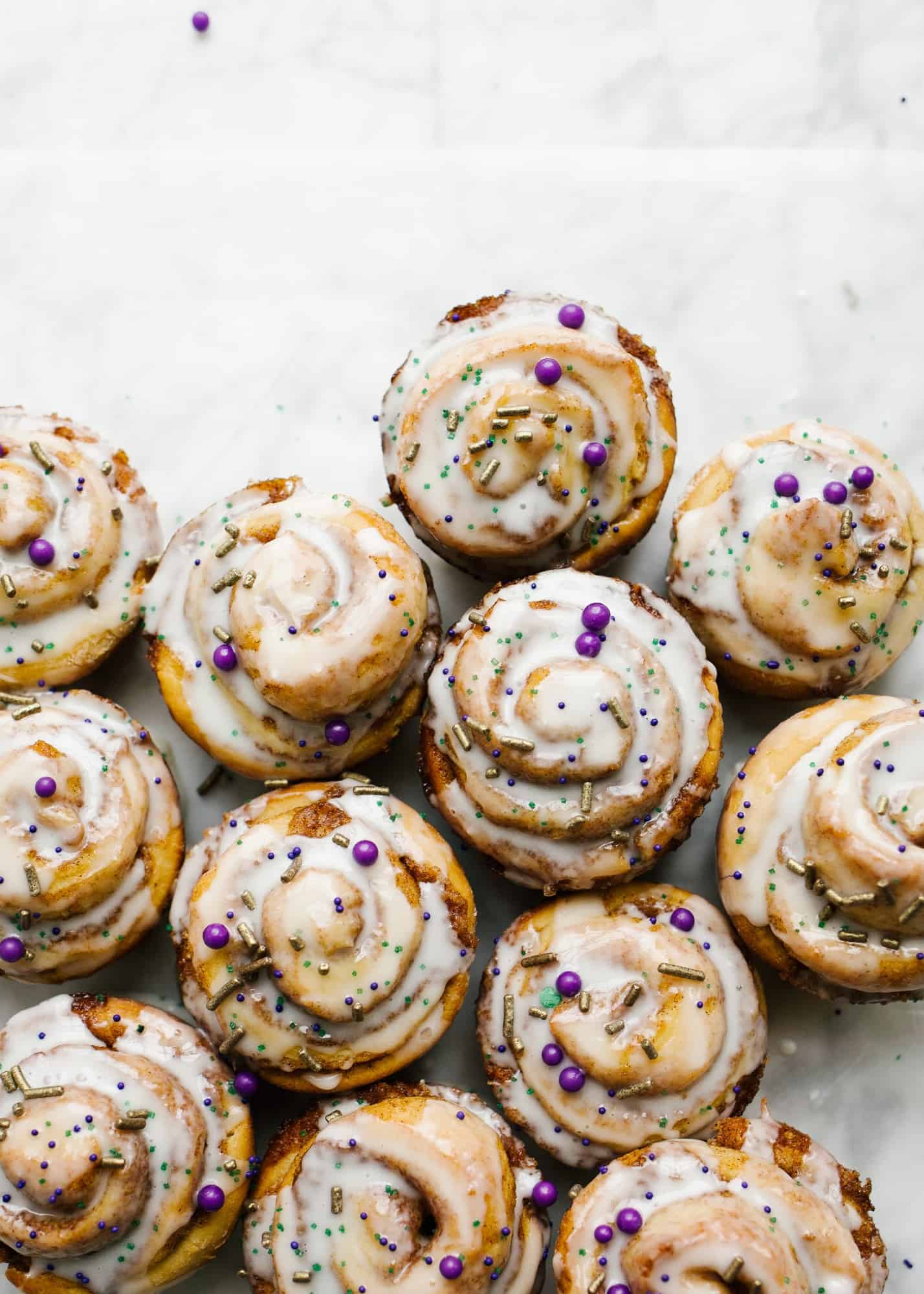 King Cake Cinnamon Rolls by Wood and Spoon blog. This is a recipe for brioche style cinnamon rolls filled with a cinnamon brown sugar filling and topped with a thick or thin powdered sugar icing glaze. Each roll is topped with festive Mardi Gras sprinkles as homage to the original king cakes! Celebrate the mardi gras season with these yummy breakfast or dessert rolls on thewoodandspoon.com