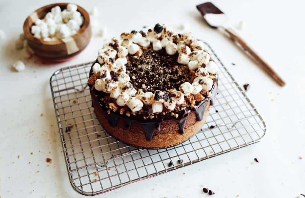 S'mores Cheesecake Recipe by The Wood and Spoon Blog by Kate Wood. This is a campfire inspired cheesecake that comes out without cracks or dry edges every time. A graham cracker, butter and sugar crust and a simple chocolate filling made from melted bars or chips. Bake the cheesecake in a water bath in the oven to get a smooth and creamy cheesecake. Top the whole thing with toasted marshmallows and more graham cracker crumbs for a summertime favorite cheesecake.