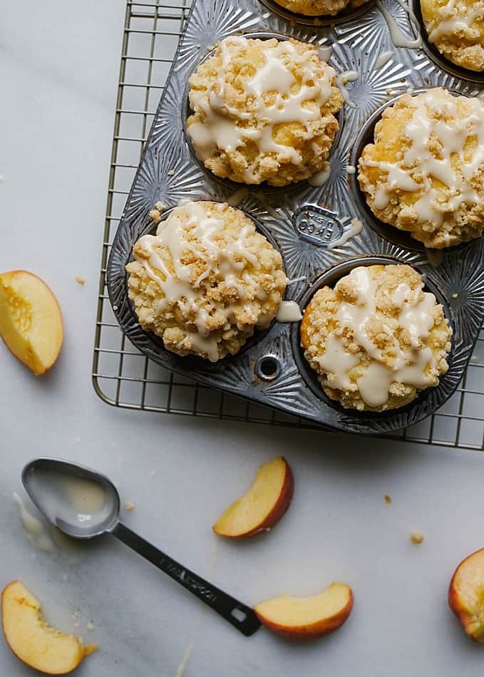 Peach Crumb Muffins Recipe By The Wood and Spoon Blog by Kate Wood. These are moist, fluffy, vanilla butter muffins filled with chunks of fresh peaches. These muffins are tall and I'll give you my tips on how to get a domed muffin every time! They are topped with a sweet and salty brown sugar streusel crumble and a dripped vanilla glaze. Find the recipe for these summer treats - the perfect breakfast or brunch item- on the blog. Thewoodandspoon.com summer fruit, beach recipes, southern muffins