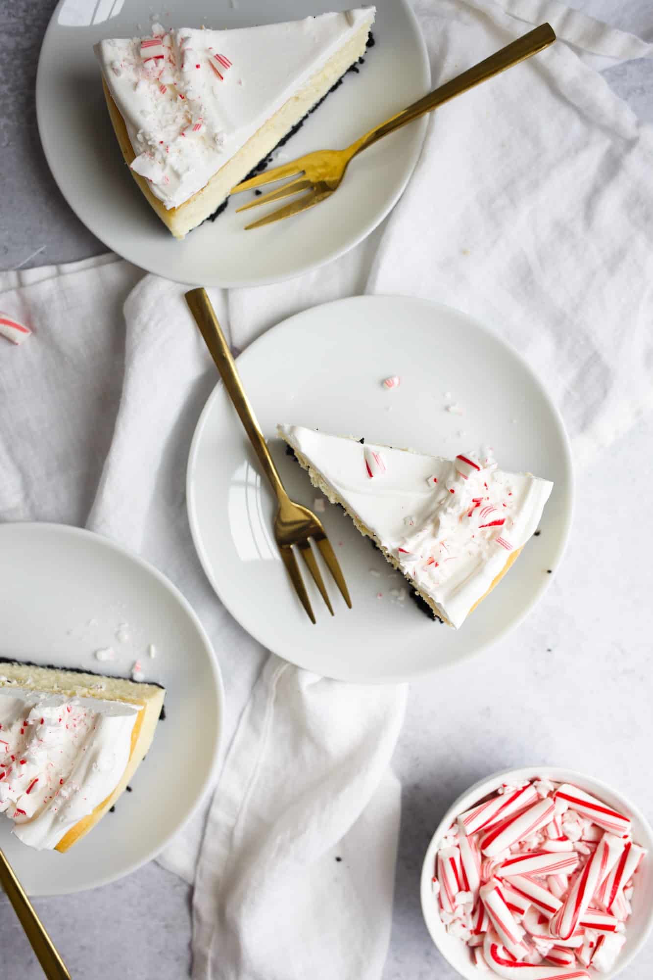 Peppermint White Chocolate Cheesecake by Wood and Spoon. This is an Oreo chocolate sandwich cookie crust cheesecake with a fluffy white chocolate peppermint filling. Topped with whipped cream and broken peppermint bark and crushed peppermint candies! Learn how to make flat pretty cheesecake on thewoodandspoon.com for holiday desserts and Christmas parties.