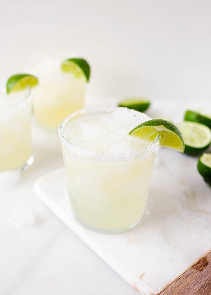 Ginger Margaritas made with a fresh spicy ginger simple syrup, fresh lime juice, and tequila blanco. These refreshing summer cocktails can be batched to serve a crowd and can easily be made ahead. Perfect poolside beverage or for serving at fiesta themed parties. Find the recipe and how-to on thewoodandspoon.com