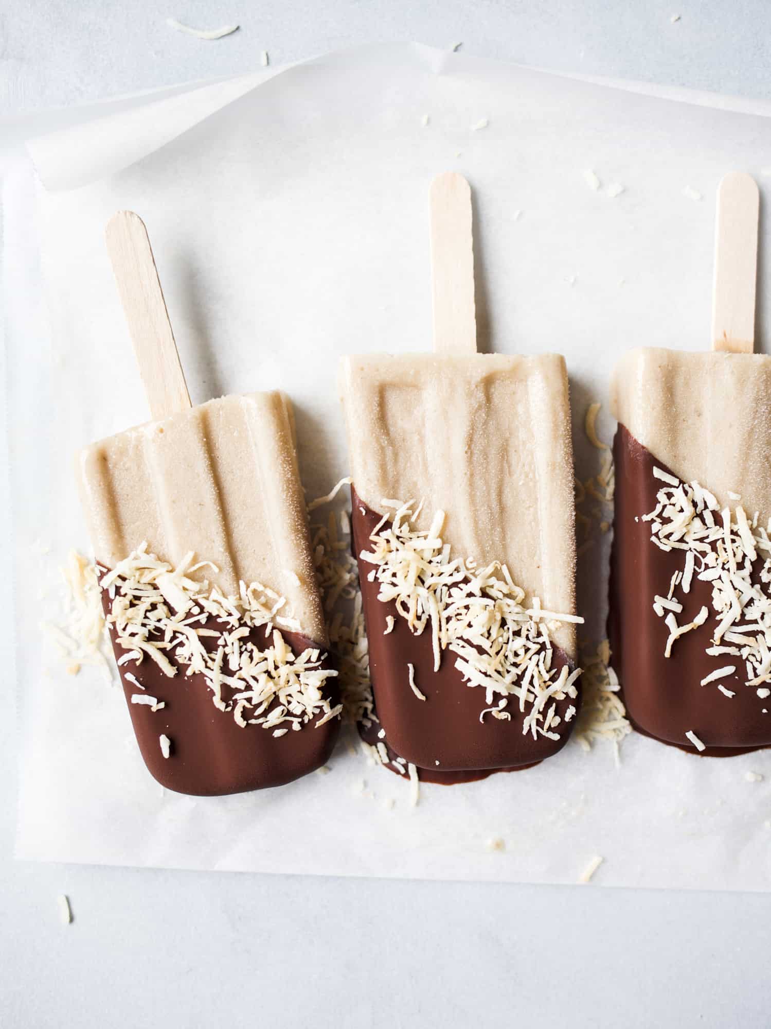 Bananas Bailey's and Coconut Popsicles Recipe by The Wood and Spoon Blog by kate Wood. This is a boozy, creamy popsicle made from Bailey's Irish cream, bananas, and cream of coconut. This frozen dessert take on the tropical beach drink is the perfect summer poptail. Boozy desserts have never been so fun and easy to make! Dip the popsicle in a magic chocolate shell and toasted coconut for a festive pretty take on these popsicles. Find the recipe and how to make homemade popsicles on thewoodandspoon.com