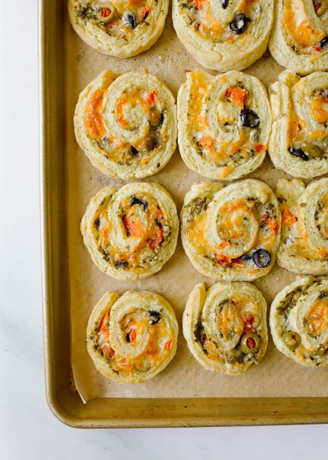 Tomato Olive Rolls by Wood and Spoon blog. These are scone like pinwheels with basil pesto, green and black olives, mozzarella and asiago cheese, and tomatoes! All of the ingredients are wrapped up in the butter and cream dough and baked until the cheese and crust are golden brown. These are similar to appetizers you can make with crescent rolls! Find the recipe and how to for these Italian mediterranean party snack foods on thewoodandspoon.com