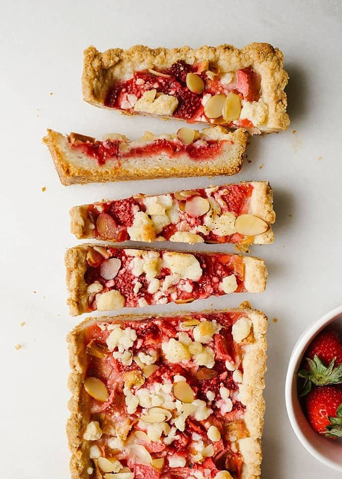 Berry Rhubarb Tart by Wood and Spoon blog. This is an almond shortbread crust tart filled with fresh strawberries and rhubarb. The remaining crust is crumbled on top of this elegant simple tart along with sliced almonds. This is a pretty dessert to make in the summer and spring and is perfect for ladies' tea or Mother's Day! Find the recipe for this pastry at thewoodandspoon.com by Kate Wood