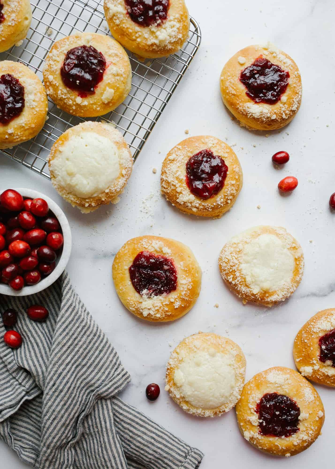 Cranberry Kolaches by Wood and Spoonn blog. These are little puffy sweat yeast parties filled with a homemade cinnamon and cranberry jam or sugared cream cheese filling. Each bite has a little simple crumble on top and is a great breakfast brunch or dessert option. Learn more about the recipe on thewoodandspoon.com.