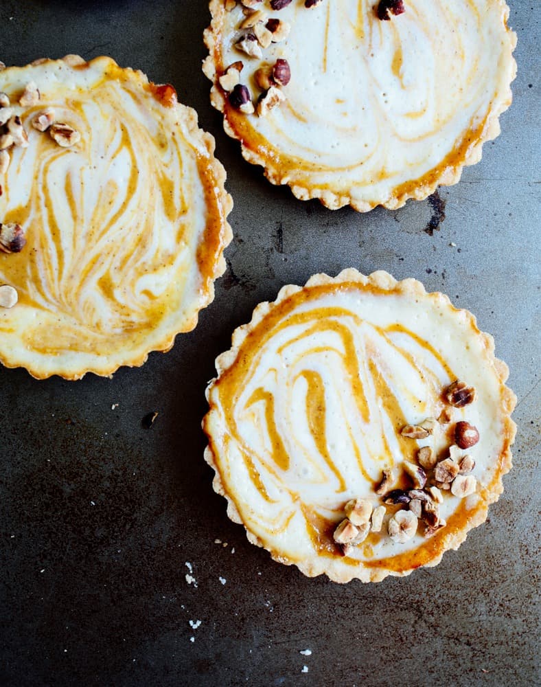 Pumpkin Cheesecake Tarts Recipe by The Wood and Spoon Blog by Kate Wood. These are simple, individual mini tarts made in removable bottom tart pans. An easy cheesecake and canned pumpkin puree filling swirled together with sugar and fall spices like cinnamon. The press in crust is easy to make and the whole thing is topped with sweet and salty walnuts or pecans or other nuts. Find this great dinner party dessert on thewoodandspoon.com