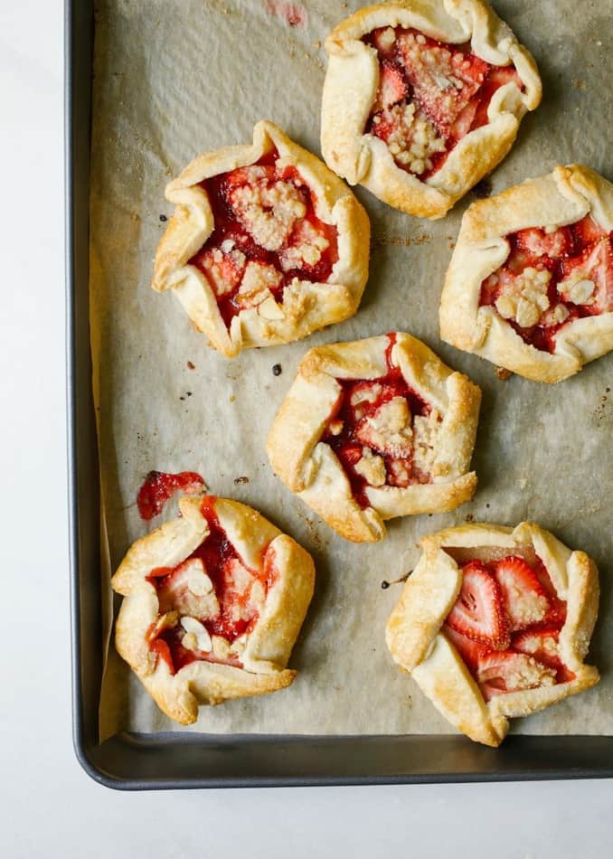 Mini Strawberry Galettes by Wood and Spoon blog. These are small open hand pies made with a simple butter dough and filled with fresh strawberries. On top an easy almond crumble adorns each dessert and a sprinkle of powdered sugar finishes them off. These little personal sized desserts are a special was to use summer produce and are sure to impress friends at parties. Find the recipe and how to on thewoodandspoon.com