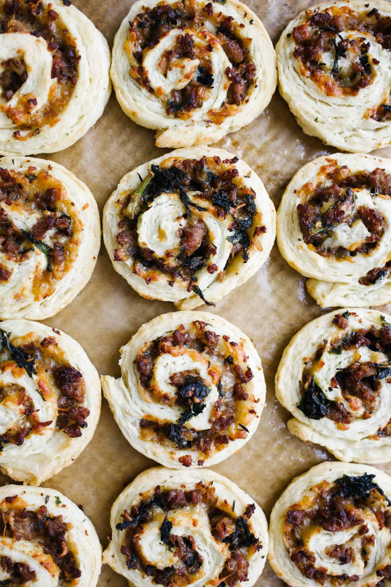 Sausage Kale Pinwheels by Wood and Spoon. These are simple pastry roll up filled with spicy italian sausage, kale, cheese, and herbs. These make great breakfast bites or afternoon snacks / appetizers. The dough is simple and requires no rising time. Think of it as a no-rise yeast dough! Learn how to make these yummy make ahead feed a crowd savory treats on thewoodandspoon.com