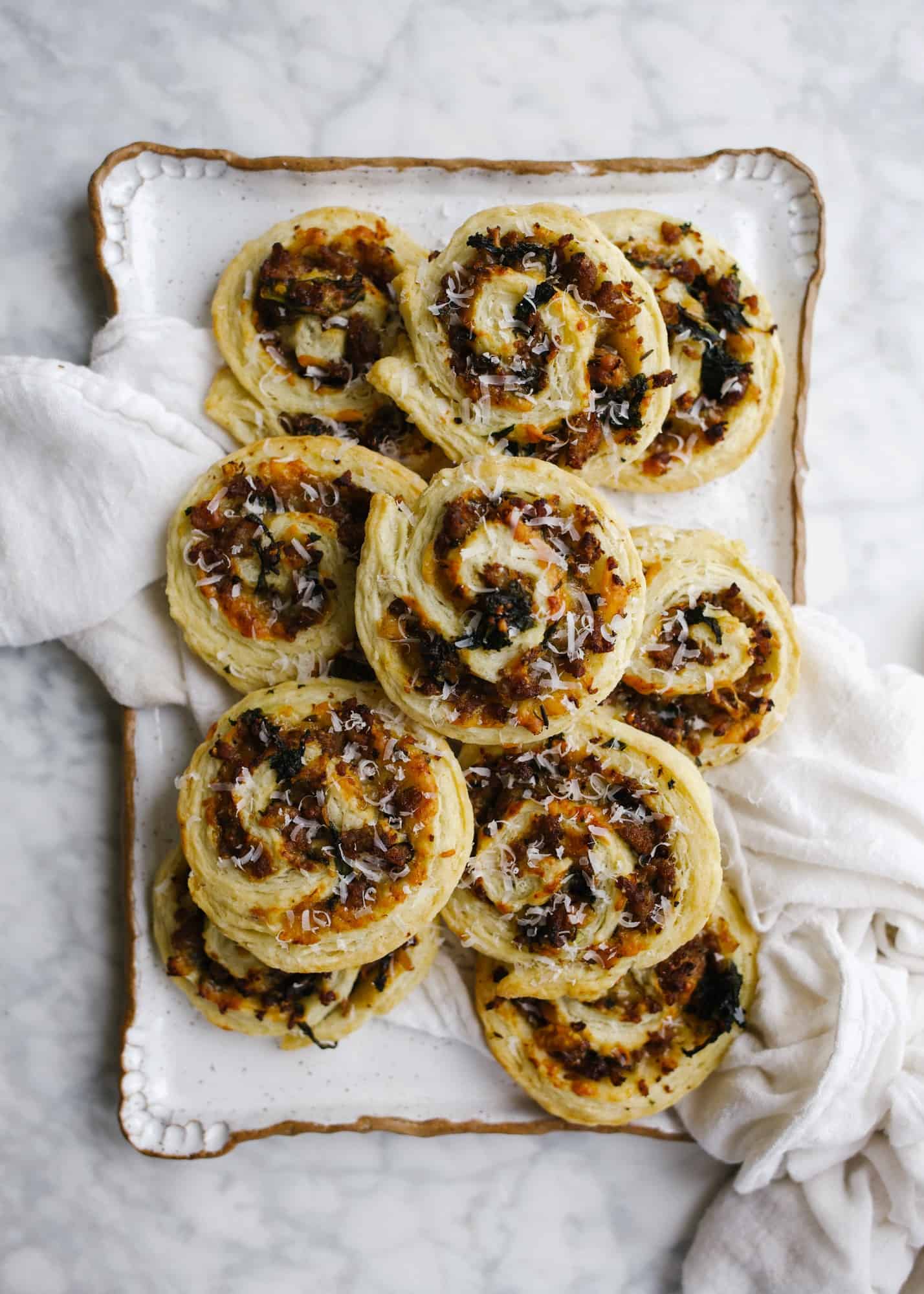 Sausage Kale Pinwheels by Wood and Spoon. These are simple pastry roll up filled with spicy italian sausage, kale, cheese, and herbs. These make great breakfast bites or afternoon snacks / appetizers. The dough is simple and requires no rising time. Think of it as a no-rise yeast dough! Learn how to make these yummy make ahead feed a crowd savory treats on thewoodandspoon.com