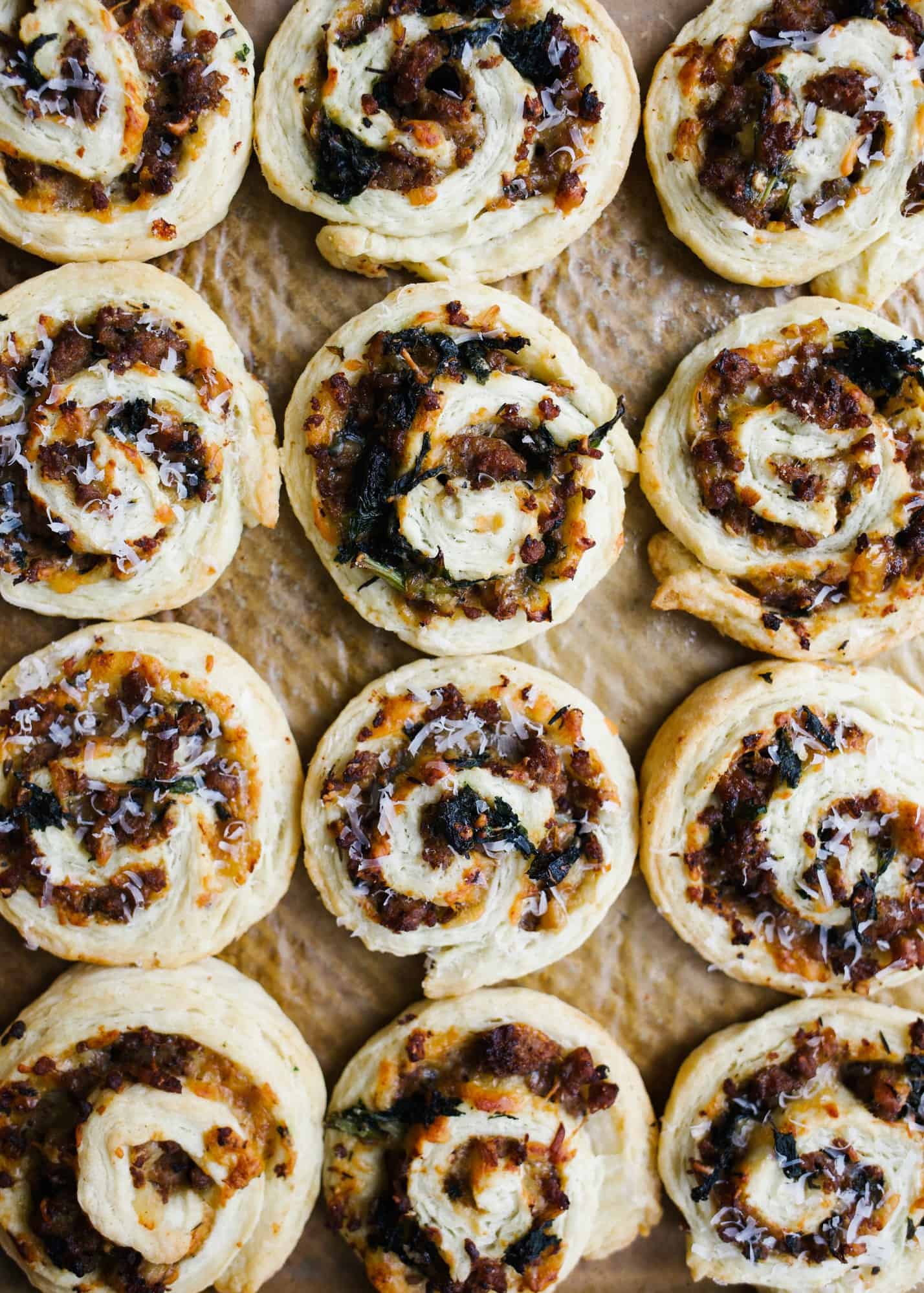 Sausage Kale Pinwheels by Wood and Spoon. These are simple pastry roll up filled with spicy italian sausage, kale, cheese, and herbs. These make great breakfast bites or afternoon snacks / appetizers. The dough is simple and requires no rising time. Think of it as a no-rise yeast dough! Learn how to make these yummy make ahead feed a crowd savory treats on thewoodandspoon.com