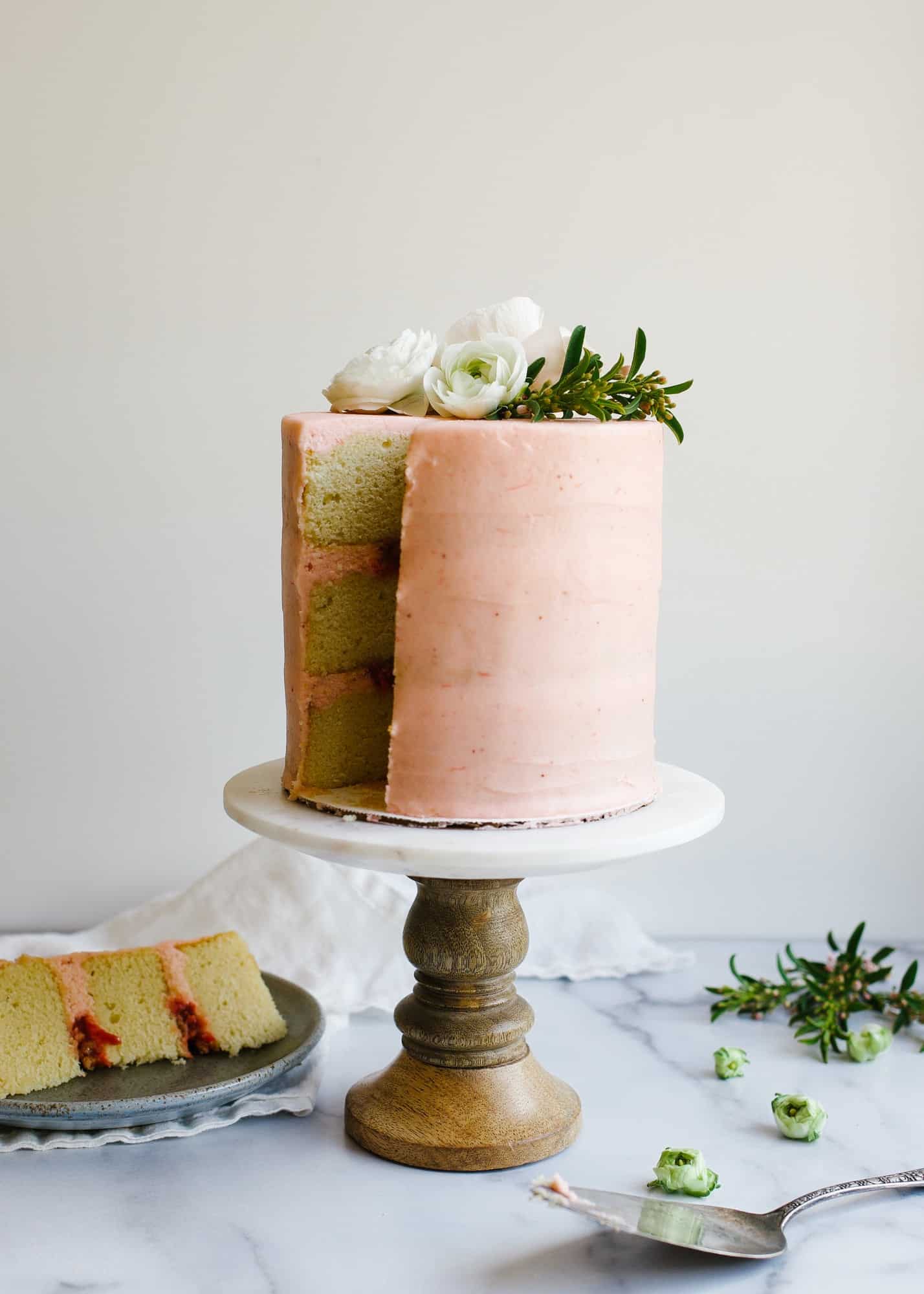 Strawberry Rhubarb Layer Cake by Wood and Spoon. These are vanilla cake layers filled with a rhubarb jam, an oatmeal streusel, and frosted with a rhubarb buttercream. This cake takes on pink color with it's fruit filled icing and stays soft and moist. Perfect for spring and summer parties and celebrations. Find out how to make this naked layer cake on thewoodandspoon.com