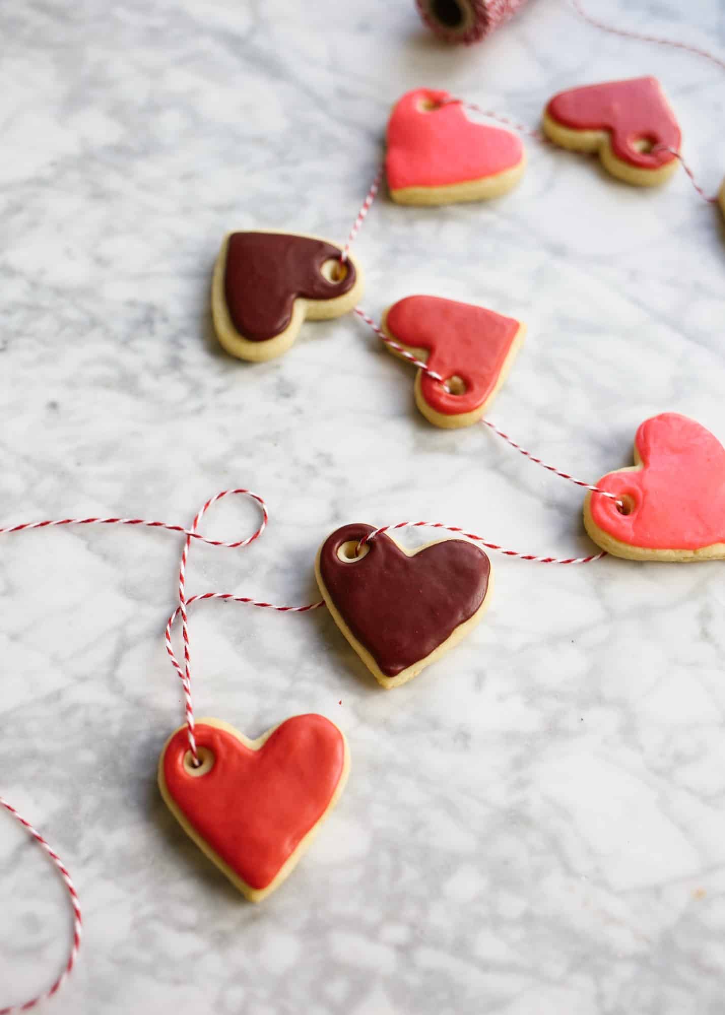 Sugar Cookie Gift Tags by Wood and Spoon blog. Use this tutorial to create, mini frosted iced heart sugar cookies to use as garland, napkin ring holders, gift tags, name tags, necklaces, and more. This simple tutorial gives you the DIY recipe for hard set cookies with homemade icing and ideas for how to use them for Valentine's Day parties, kid crafts, and more. Read about the recipe and how to on thewoodandspoon.com by Kate Wood