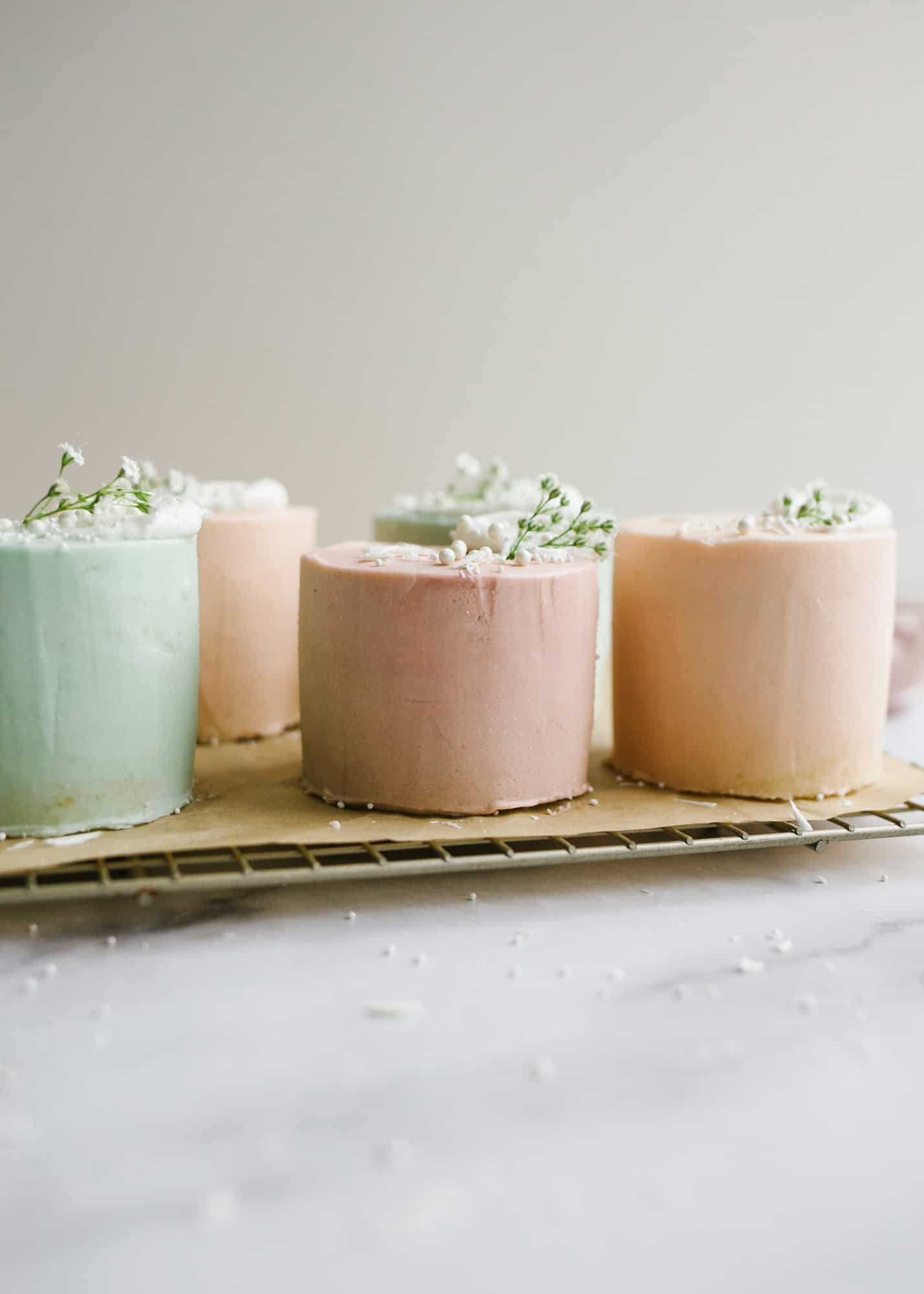 Mini Layer Cakes by Wood and Spoon blog. These are tiny three layer pastel cakes perfect for parties, spring holidays, and Mother's Day. The small vanilla cakes are baked in a sheet pan and then frosted together with a simple American buttercream. The cakes are colored in pale easter colors and served as individual desserts. Perfect mini cake for two. Find the recipe and how to on thewoodandspoon.com by Kate Wood