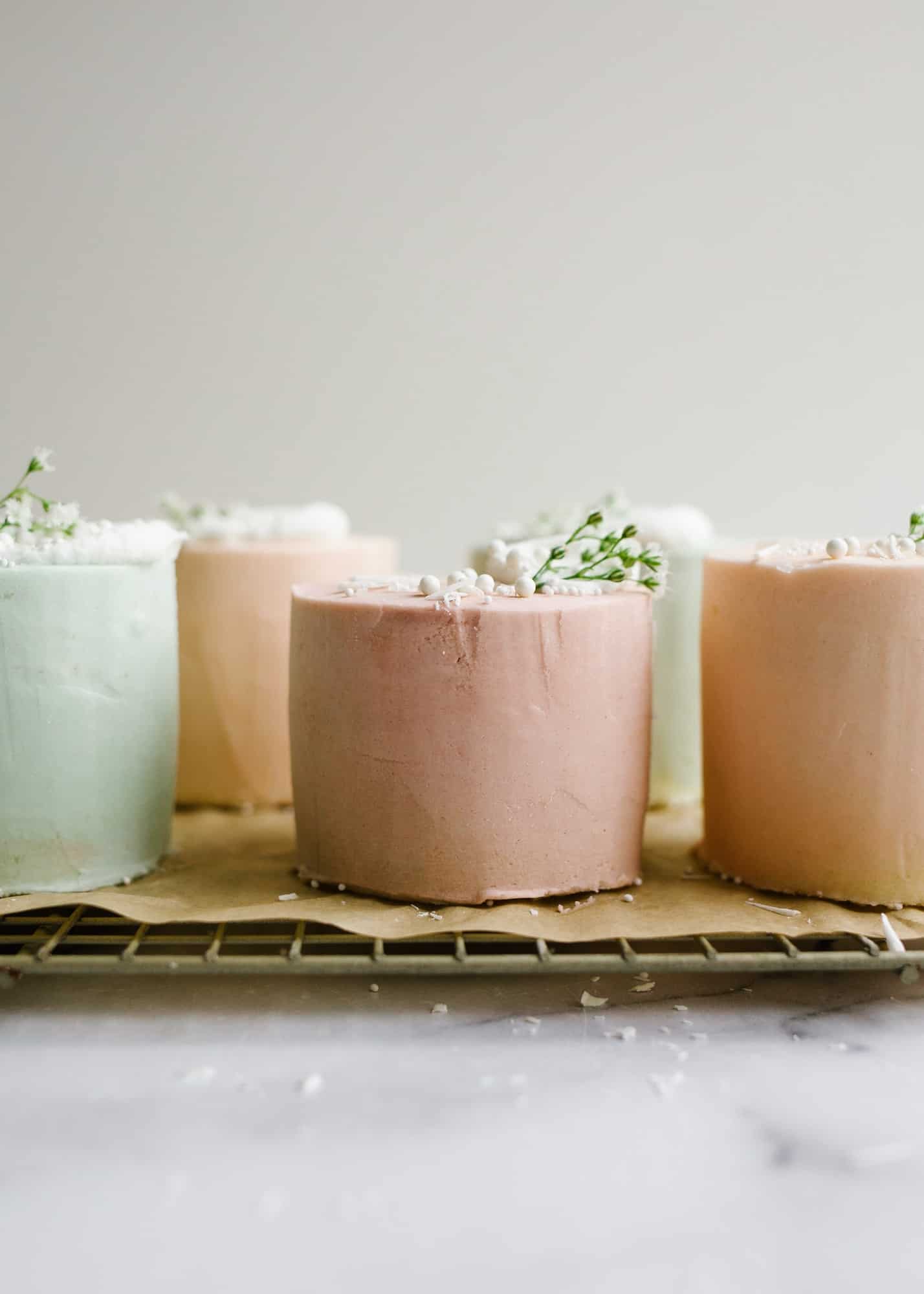 Mini Layer Cakes by Wood and Spoon blog. These are tiny three layer pastel cakes perfect for parties, spring holidays, and Mother's Day. The small vanilla cakes are baked in a sheet pan and then frosted together with a simple American buttercream. The cakes are colored in pale easter colors and served as individual desserts. Perfect mini cake for two. Find the recipe and how to on thewoodandspoon.com by Kate Wood