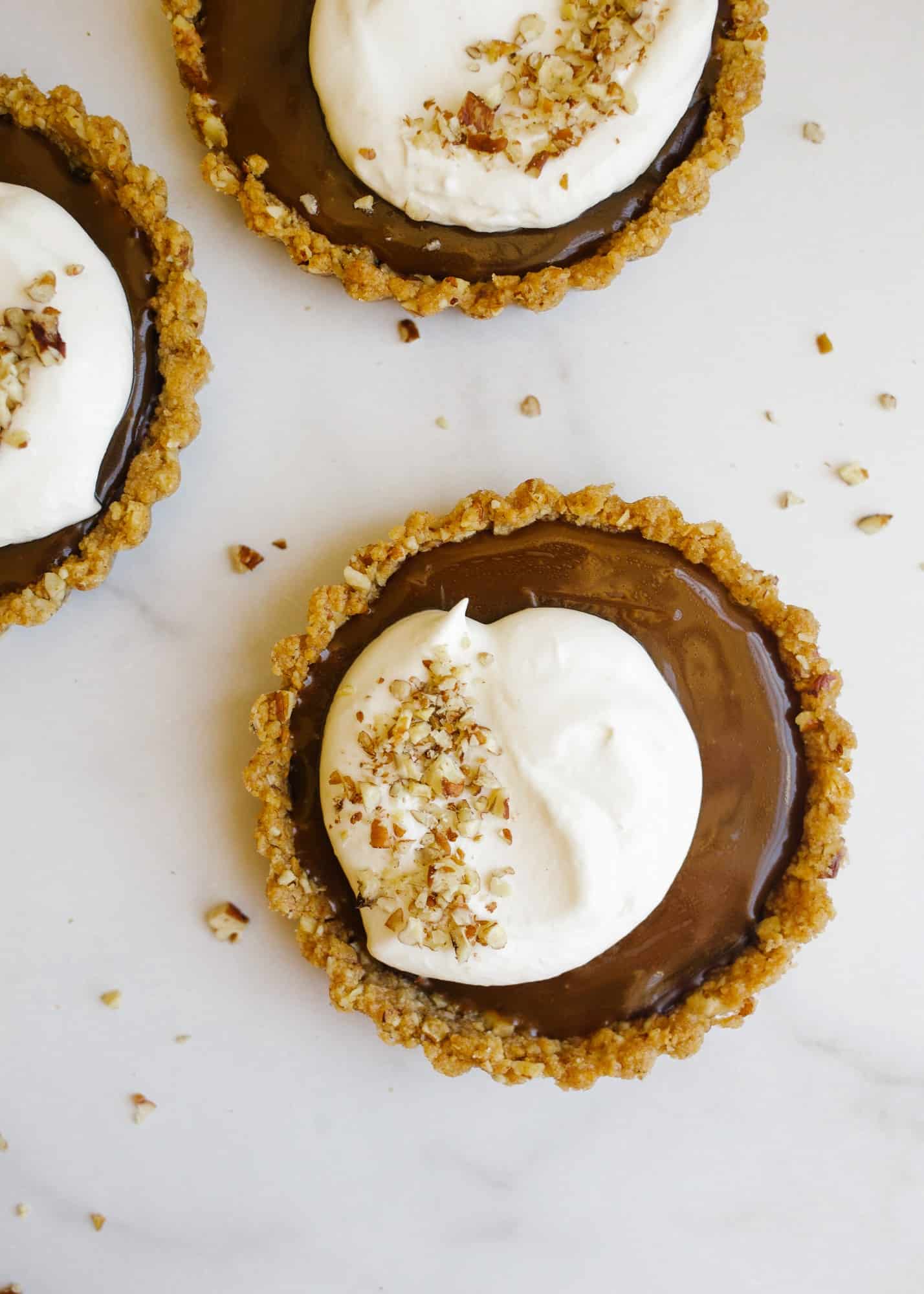 Chocolate Caramel Pecan Tarts by Wood and Spoon blog. These are pecan graham cracker crusted mini tartlets filled with a dark chocolate ganache, a salted caramel sauce, whipped cream, and toasted pecans. THe recipe makes 4 mini desserts fun for parties and are a rich sweet and salty treat for all year round. Almost no bake and simple to make! Find the recipe on thewoodandspoon.com