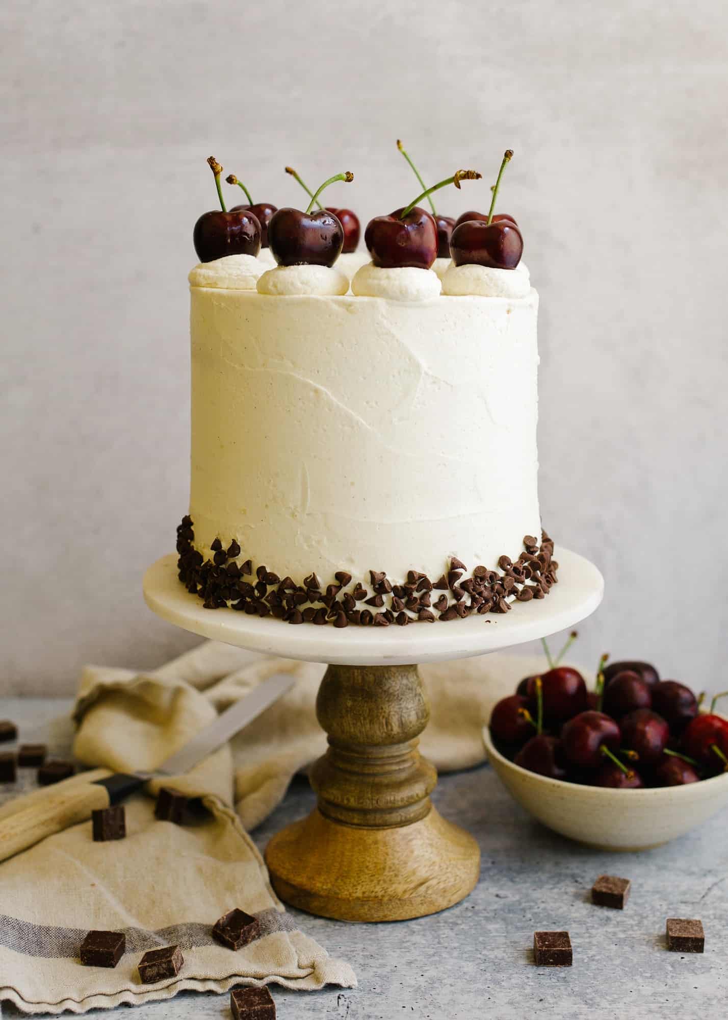 Cherry Chip Cake recipe by wood and spoon. This is a vanilla cake with cherries and mini chocolate chips filled with a quick dark cherry filling and coated with a tangy cream cheese American buttercream. The cake is a great summer layer cake for parties and cake be made in advance. The frosting is stable and compliments the cherries and chocolate well. Find the recipe and learn more about stacking layer cakes on thewoodandspoon.com