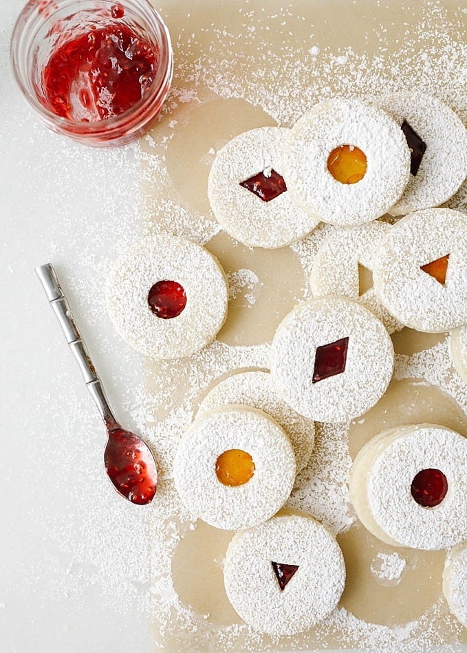 Raspberry Lemon Linzer Cookies recipe by The Wood and Spoon blog by Kate Wood. This is a classic linzer cookie recipe made with almond flour and all-purpose flour. The cookies are scented with lemon zest and are filled with a raspberry jam. The dough is cut out with cookie cutters. Sprinkle the tops of these Christmas baked goods with powdered sugar. These are what to bring to holiday or Christmas party / exchange. Find the recipe and the how to on thewoodandspoon.com