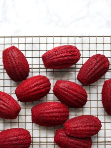 Red Velvet Madeleines By Wood and Spoon Blog. These are cocoa-scented French cookies dipped in a cream cheese glaze and decorated with sprinkles. Learning how to make French madeleines with a big hump is easy and this recipe makes red velvet madeleines delicious and fun. Find this perfect holiday recipe on the woodandspoon.com