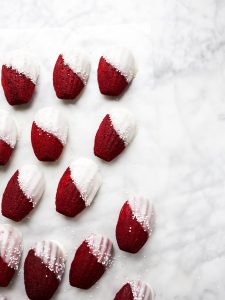 Red Velvet Madeleines By Wood and Spoon Blog. These are cocoa-scented French cookies dipped in a cream cheese glaze and decorated with sprinkles. Learning how to make French madeleines with a big hump is easy and this recipe makes red velvet madeleines delicious and fun. Find this perfect holiday recipe on the woodandspoon.com