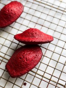 Red Velvet Madeleines By Wood and Spoon Blog. These are cocoa-scented French cookies dipped in a cream cheese glaze and decorated with sprinkles. Learning how to make French madeleines with a big hump is easy and this recipe makes red velvet madeleines delicious and fun. Find this perfect holiday recipe on the woodandspoon.com