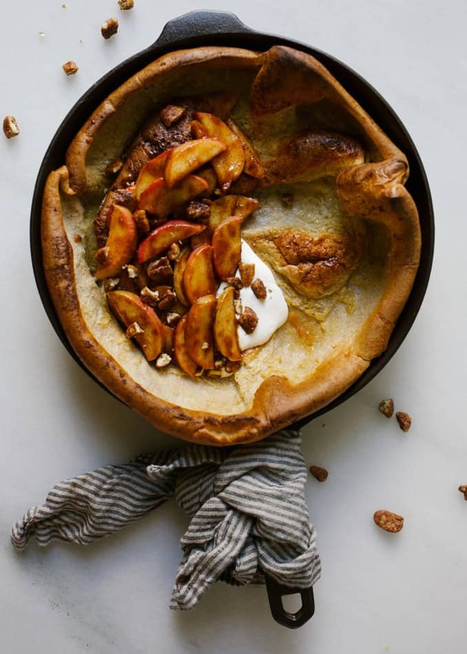 Pecan Apple Dutch Baby by Wood and Spoon. This is a cinnamon flavored skillet pancake topped with cinnamon spiced apples and maple glazed pecans. This one bowl recipe can be make in a pinch and is a fun breakfast to make with kids. Watch this simple treat rise In the oven and top it with fall-flavored fruit and crunchy, sweet and salty nuts. Find the recipe and how-to on thewoodandspoon.com