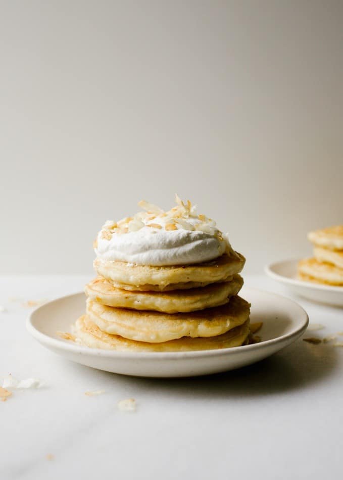 Almost Vegan Coconut White Chocolate Pancakes recipe by Wood and spoon. These are coconut oil pancakes sweetened with dried flaked coconut and white chocolate! The pancakes are light and fluffy and flavored with coconut thanks to the coconut milk. Top with coconut whipped cream or fresh fruit compote for a delicious healthy breakfast that actually heat well too! Find this vegetarian recipe on thewoodandspoon.com brunch