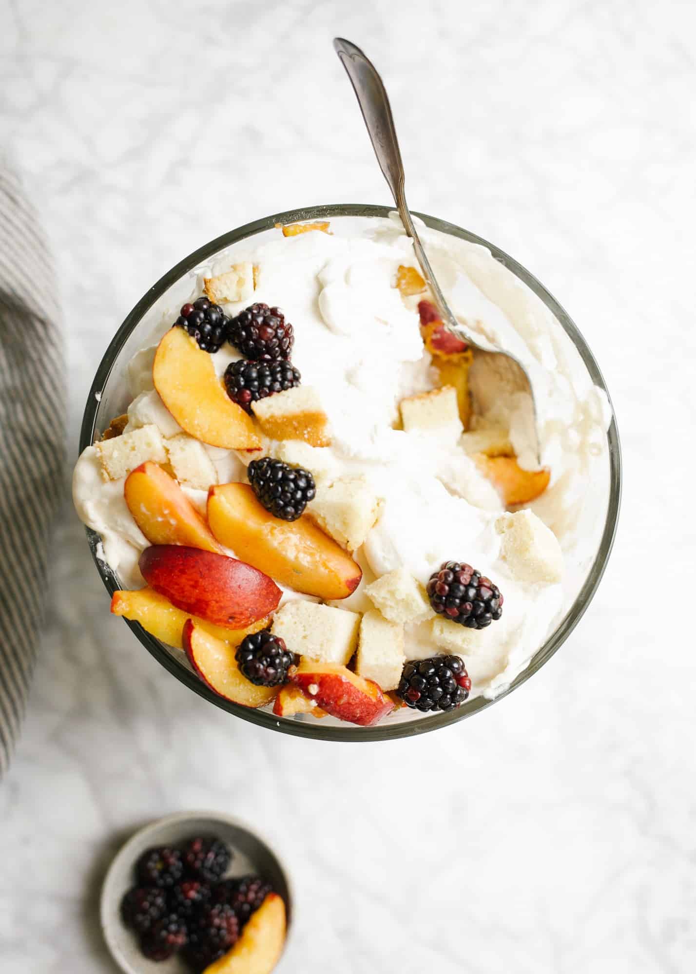 Peaches and Cream Trifle by Wood and Spoon blog. This trifle features homemade pound cake, a cream cheese whipped cream, and fresh sugared summer peaches. Add a few berries or you other favorite summer fruit to make this a festive and colorful dessert to serve a crowd for warm weather gatherings. You can make this ahead or use store-bought pound cake! Find more about the recipe on thewoodandspoon.com