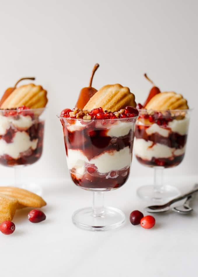 Poached Pear Trifles with wine pears, cranberries, pomegranate, Donsuemor madeleines and a creamy whipped filling. These trifles are sweet and tangy and boozy all at the same time. First up are red wine and cinnamon poached pears and cranberries that are cooked until soft. These are layered with a cream cheese or mascarpone whipped filling scented with orange zest, French madeleines, and more fresh fruit! Make these treats for a fancy holiday gathering. You can make large trifles or smaller individual ones. Recipe on thewoodandspoon.com by Kate Wood