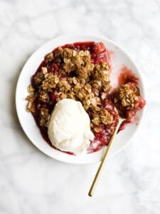 Strawberry Rhubarb Crisp by Wood and Spoon blog. This is a simple fresh summer fruit crisp made in a cast-iron skillet and served with vanilla ice cream. Oats, brown sugar, and butter make up the crumble topping of this potluck dessert that serves a crowd. Learn how to make this yummy fruit dessert and how to use rhubarb on thewoodandspoon.com.