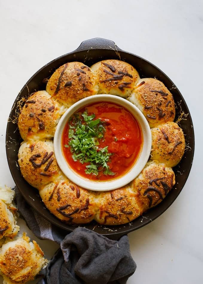 Cheesy Dinner Rolls with Tomato Dipping Sauce recipe by wood and spoon. These are soft and fluffy yeast rolls filled with gooey mozzarella cheese. Baked in a skillet and topped with italian herbs and cheese, these rolls serve as a great appetizer, side dish, and more! Make your holiday bread bowls extra delicious with these stuffed yeast breads! Check it out on thewoodandspoon.com