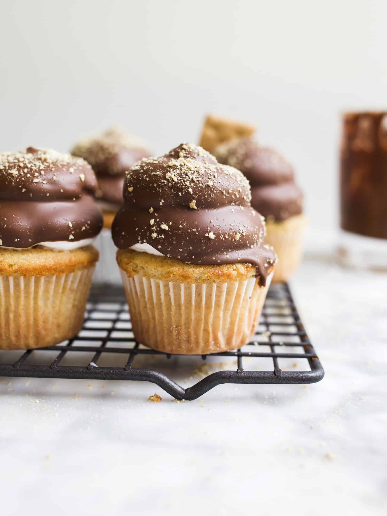 S'mores Hi-Hat Cupcakes by Wood and Spoon blog. These are graham cracker cupcakes topped with a marshmallow topping and dipped in a milk chocolate shell. These cupcakes taste like s'mores and are a beautiful way to feature chocolate magic shell. Learn how to make them on thewoodandspoon.com