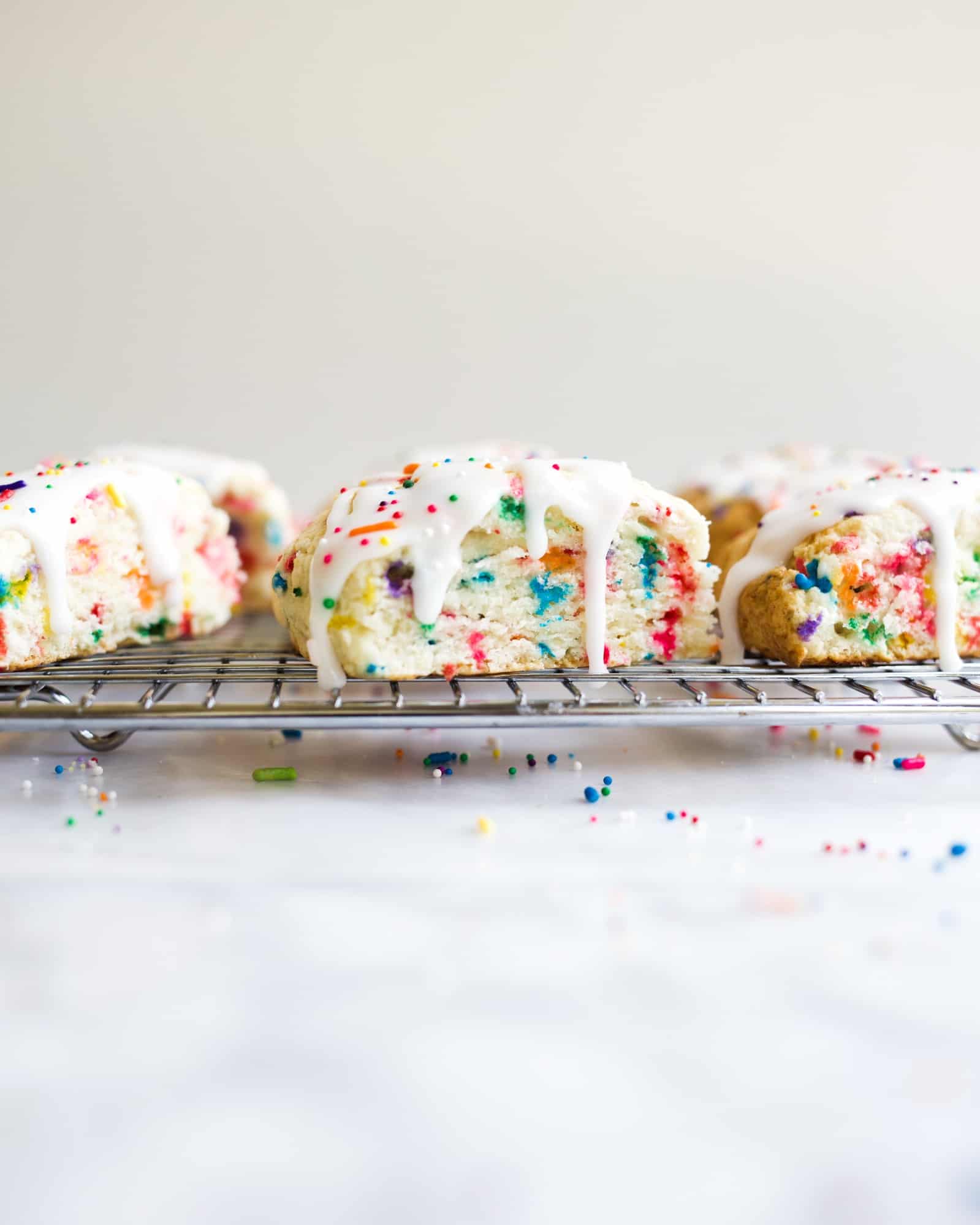 Funfetti Scones Recipe by The Wood and Spoon Blog by Kate Wood. Simple, fast, easy one bowl cream scones that taste just like a box mix birthday cake! These scones use clear vanilla and sprinkles to make the sweet confetti flavor. The icing is a simple powdered sugar glaze speckled with more rainbow jimmies. Find the Recipe on thewoodandspoon.com along with more breakfast or brunch ideas to go with your coffee and tea time!