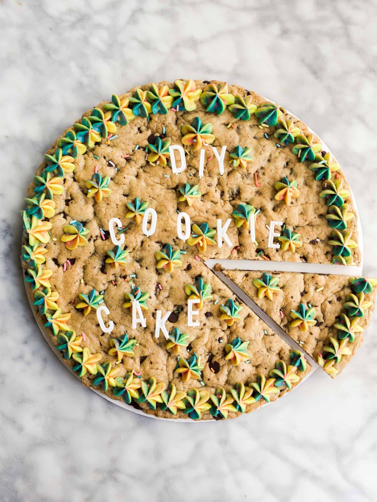 DIY Cookie Cake by Wood and Spoon Blog. This is a recipe for a homemade cookie cake, similar in flavor to the cult favorites from Great American Cookie Company! This giant chewy chocolate chip cookie is frosted with a simple one-bowl American buttercream, and the entire dessert comes together in less than 30 minutes. Find the simple recipe on thewoodandspoon.com