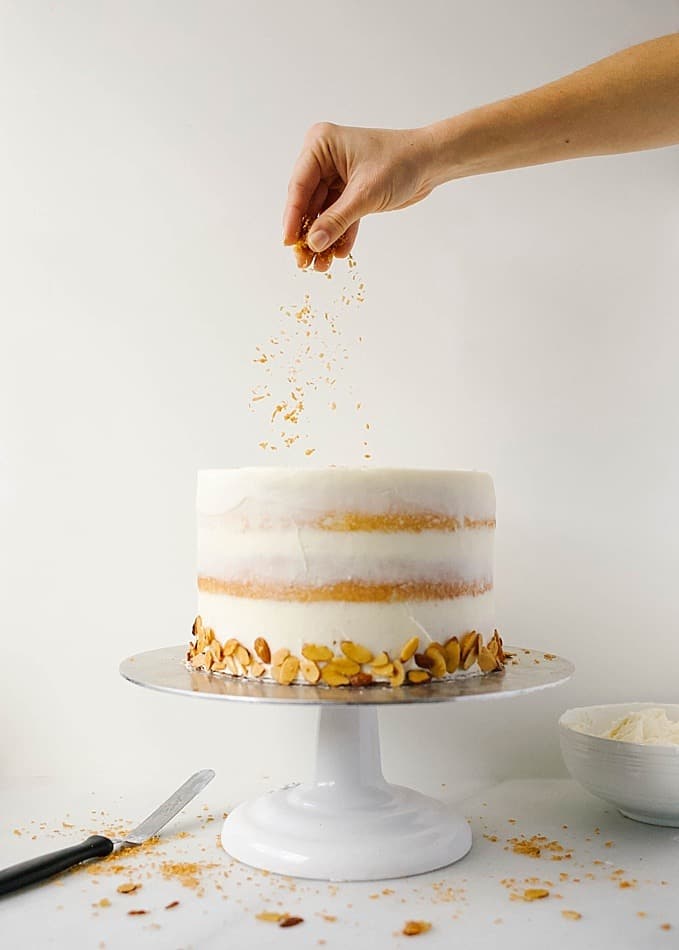 Almond Coconut Cake recipe by Wood and Spoon Blog by Kate Wood. This is a recipe for a sweet and fluffy almond layer cake, speckled with flakes of sweetened coconut and frosted with a coconut American buttercream. The whole thing is topped with extra toasted coconut and almond, a cake that is as beautiful as it is delicious. This layer cake is simple and easy to make, and learning how to make stacked naked cakes is fun! Find the recipe for this Easter / spring cake on thewoodandspoon.com